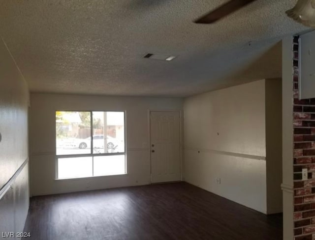 unfurnished room featuring brick wall, a textured ceiling, and dark hardwood / wood-style floors