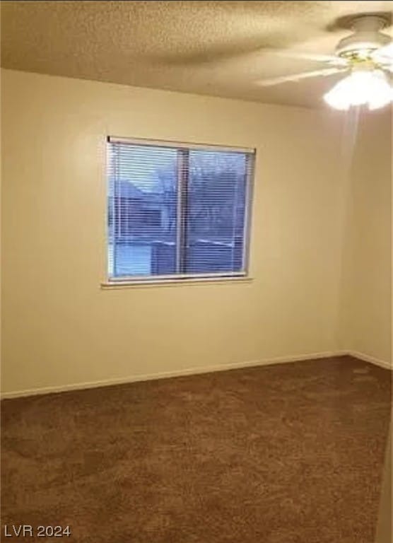 spare room with a textured ceiling, ceiling fan, and dark colored carpet