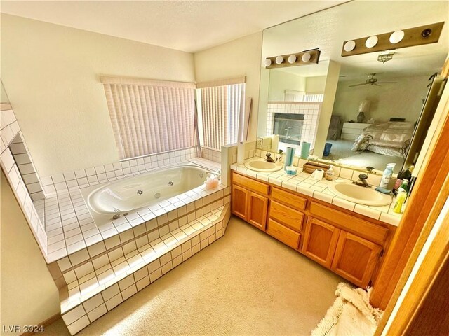 bathroom with tiled tub, vanity, and ceiling fan