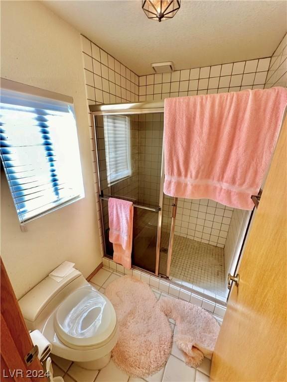 bathroom with a textured ceiling, tile patterned flooring, toilet, and a shower with shower door