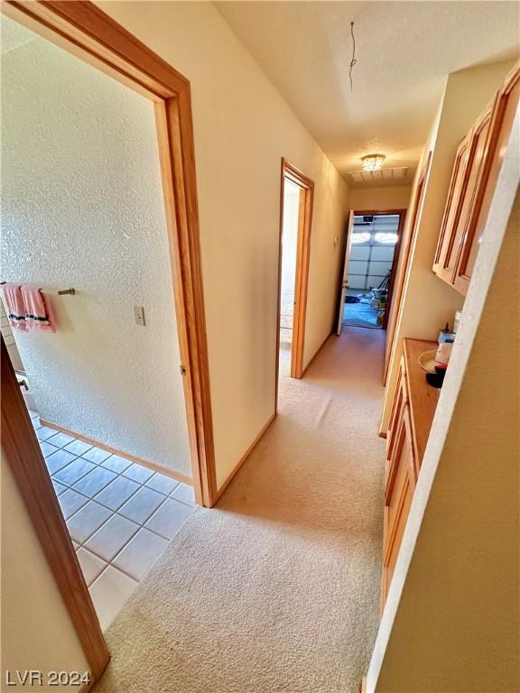 hall featuring light tile patterned floors, light colored carpet, baseboards, and a textured wall