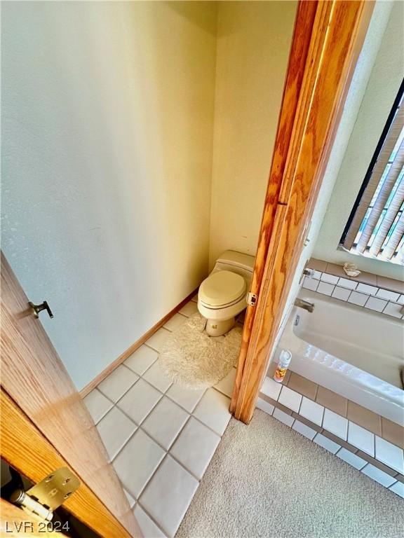 full bath with tile patterned flooring, a washtub, toilet, and baseboards