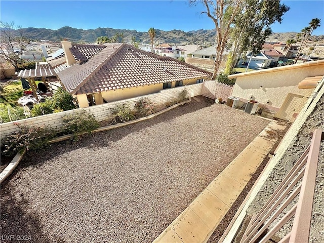 view of side of home with a tile roof, a patio, a fenced backyard, a mountain view, and a flat roof