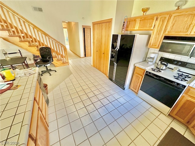 kitchen featuring visible vents, light brown cabinets, tile counters, white range with gas stovetop, and black fridge with ice dispenser