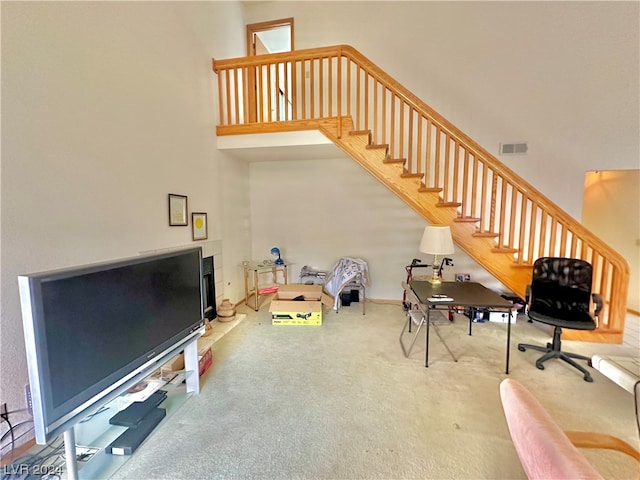 interior space with visible vents, a fireplace with raised hearth, stairway, carpet floors, and a high ceiling