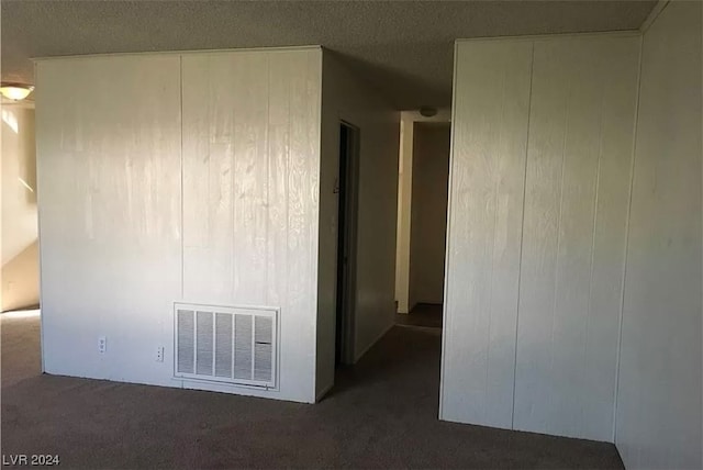 unfurnished room featuring dark colored carpet and a textured ceiling