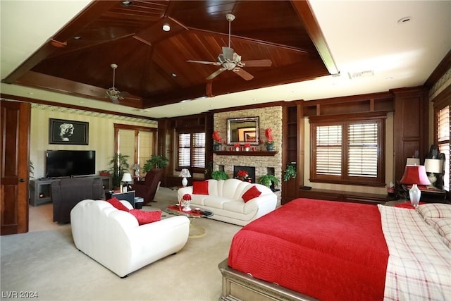 carpeted bedroom with a stone fireplace, ceiling fan, wood ceiling, and a raised ceiling