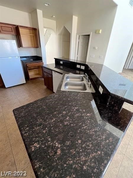 kitchen with white appliances, sink, light tile floors, and dark stone counters