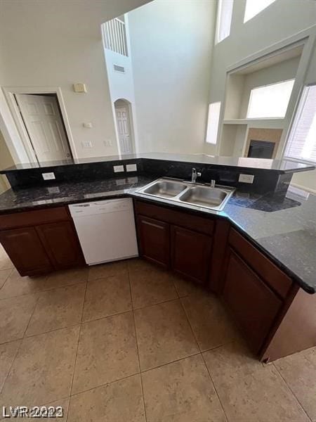 kitchen with light tile flooring, sink, dark stone countertops, dishwasher, and dark brown cabinets