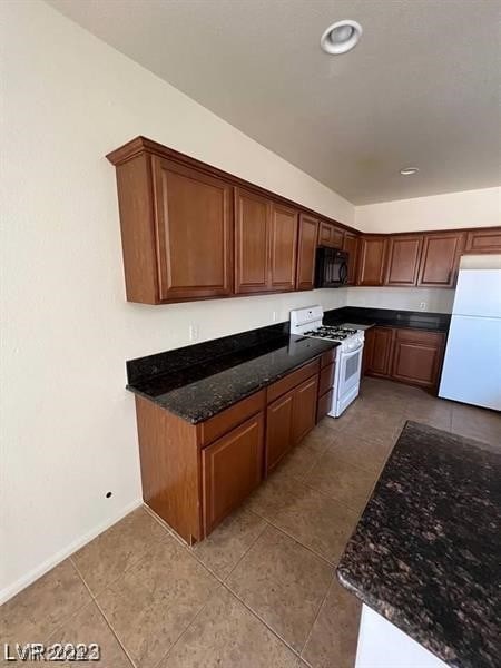 kitchen with white appliances, light tile floors, and dark stone counters