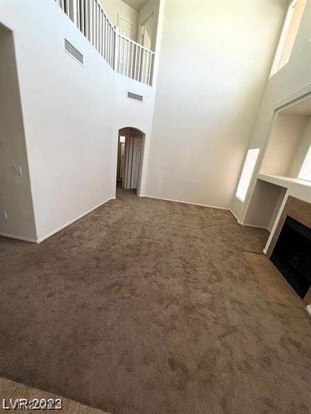 unfurnished living room featuring dark carpet and a towering ceiling