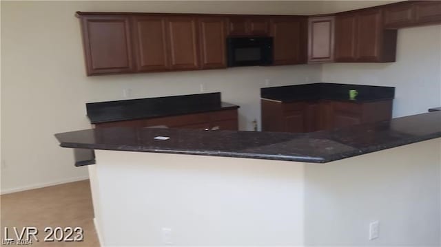 kitchen featuring dark stone countertops, dark brown cabinets, and kitchen peninsula