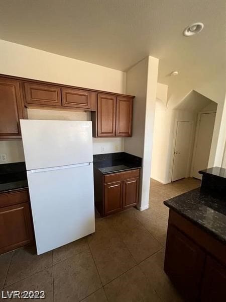 kitchen with dark stone countertops, dark tile floors, and white fridge