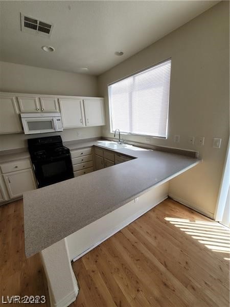 kitchen with kitchen peninsula, light hardwood / wood-style flooring, sink, white cabinetry, and black stove