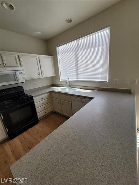 kitchen featuring wood-type flooring, white cabinetry, stainless steel dishwasher, sink, and gas stove