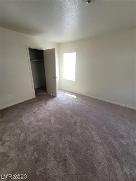 unfurnished bedroom with dark colored carpet, a textured ceiling, and a closet