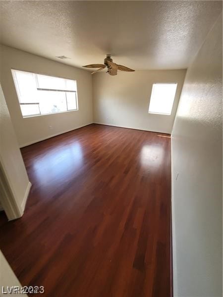 empty room featuring ceiling fan, a wealth of natural light, dark hardwood / wood-style floors, and a textured ceiling