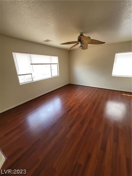 unfurnished room with dark wood-type flooring, a textured ceiling, a healthy amount of sunlight, and ceiling fan