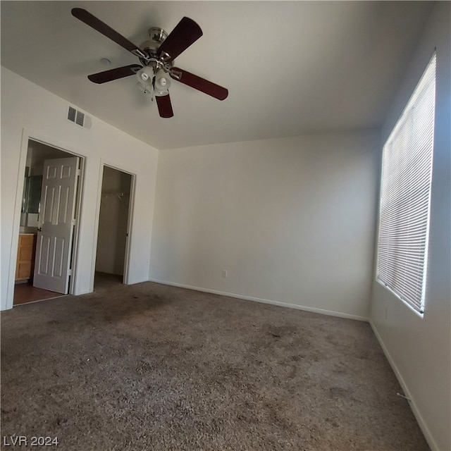 unfurnished bedroom with dark colored carpet, ensuite bathroom, ceiling fan, a closet, and a walk in closet