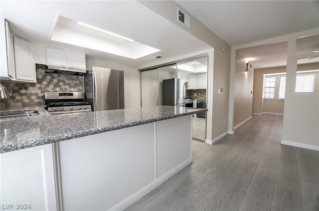 kitchen featuring stainless steel appliances, light wood-type flooring, white cabinetry, backsplash, and dark stone countertops