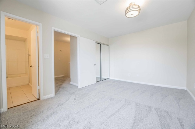 unfurnished bedroom featuring a closet, light colored carpet, and ensuite bathroom