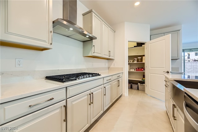 kitchen with light tile patterned floors, white cabinets, stainless steel appliances, and wall chimney range hood