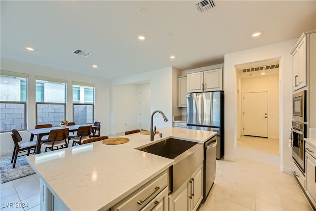 kitchen featuring light stone countertops, appliances with stainless steel finishes, a kitchen island with sink, sink, and white cabinets