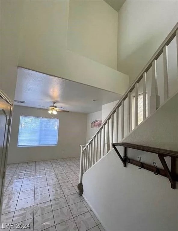 staircase with light tile floors, ceiling fan, and a towering ceiling