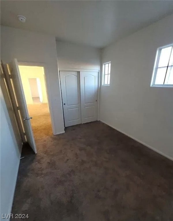 unfurnished bedroom with dark carpet and a closet