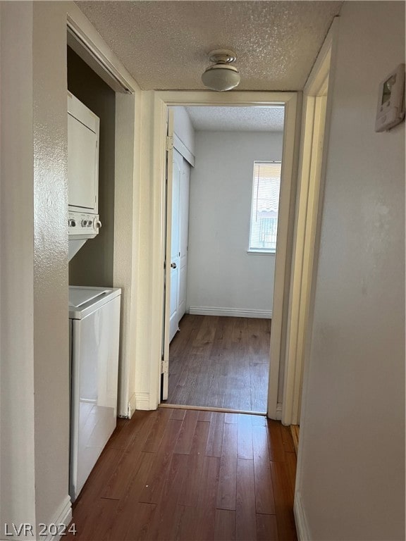 hallway featuring stacked washing maching and dryer, a textured ceiling, and dark hardwood / wood-style flooring