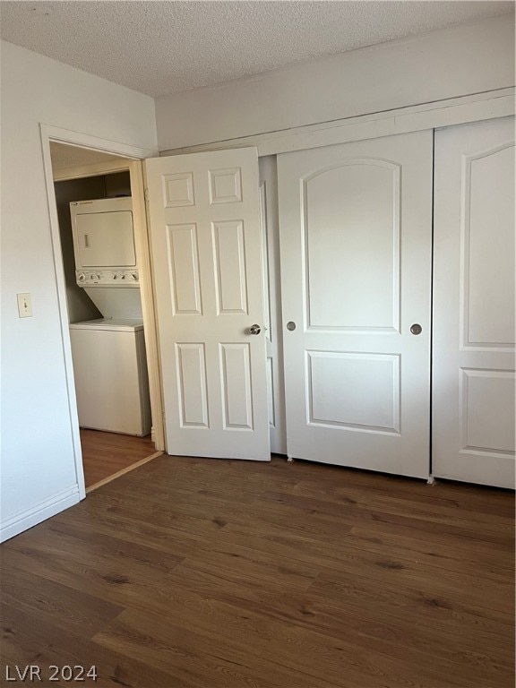 unfurnished bedroom featuring a textured ceiling, dark hardwood / wood-style flooring, a closet, and stacked washing maching and dryer