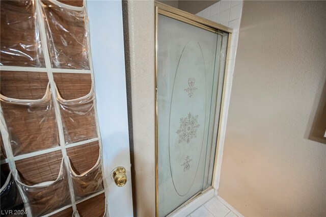 interior details with a shower with shower door and light tile floors