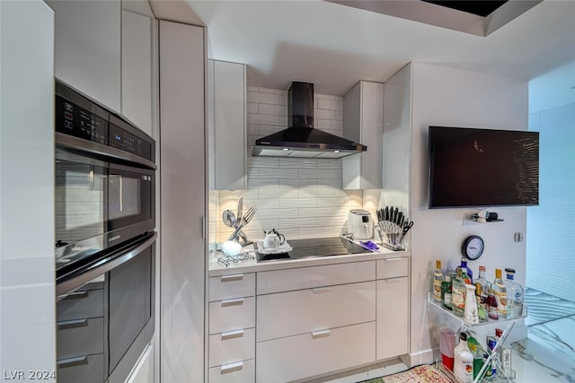 kitchen with tasteful backsplash, black electric stovetop, stainless steel double oven, wall chimney exhaust hood, and white cabinets