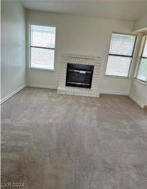 unfurnished living room featuring a brick fireplace, a wealth of natural light, and light carpet