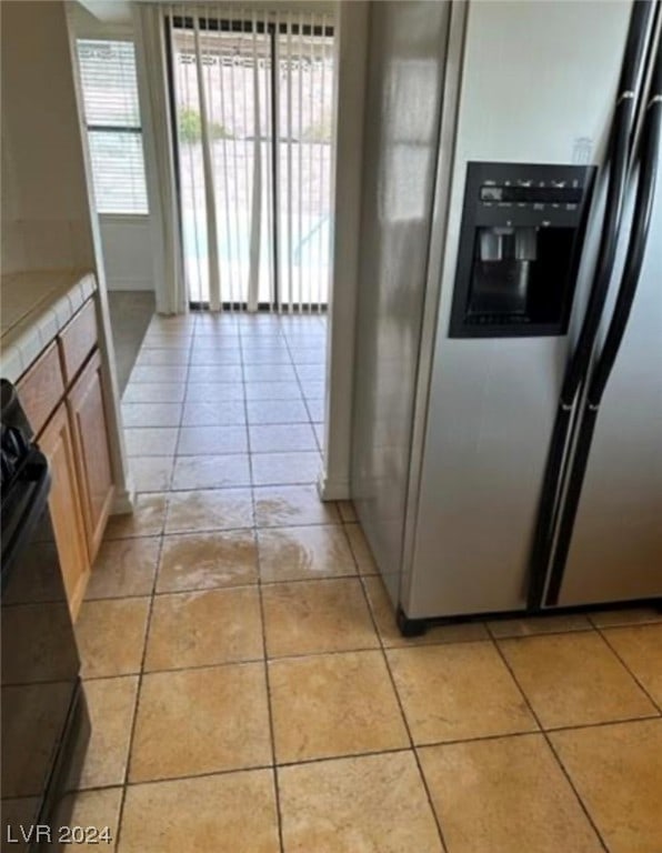 kitchen with light brown cabinets, stainless steel fridge with ice dispenser, light tile floors, and black electric range