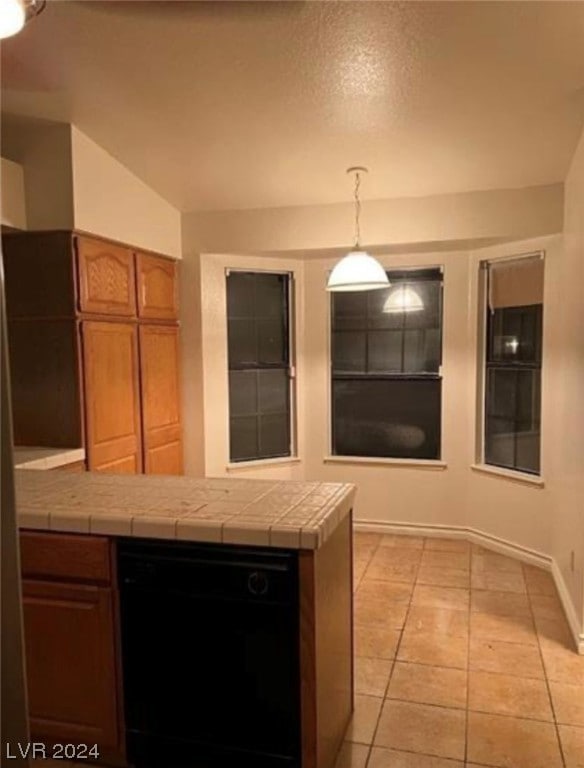 kitchen featuring black dishwasher, hanging light fixtures, tile countertops, and light tile floors