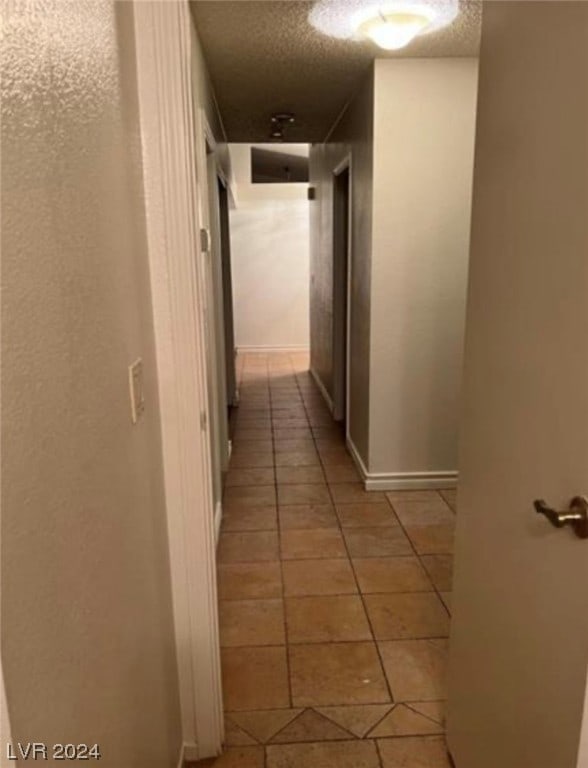 corridor with light tile flooring and a textured ceiling