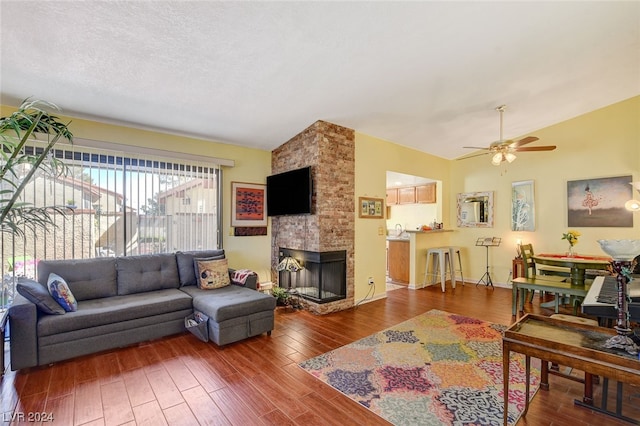 living room featuring dark wood-type flooring, ceiling fan, brick wall, a fireplace, and vaulted ceiling