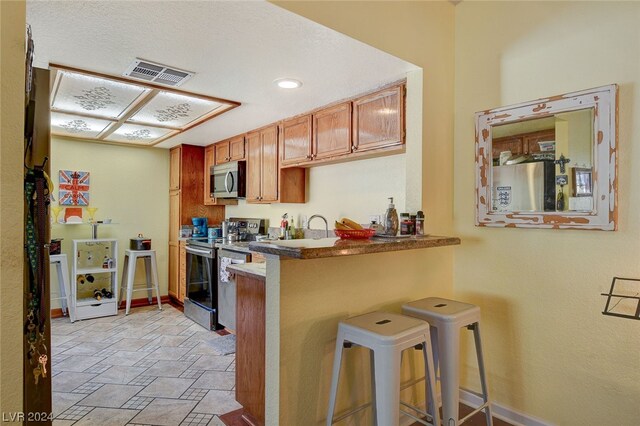 kitchen featuring light tile floors, range with electric stovetop, kitchen peninsula, and a breakfast bar