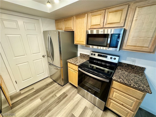 kitchen with light brown cabinets, stainless steel appliances, light wood-type flooring, and dark stone countertops