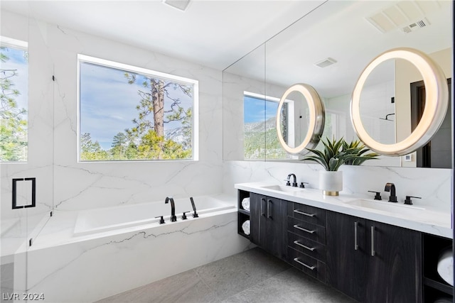 bathroom with tile walls, tile floors, tiled bath, large vanity, and dual sinks