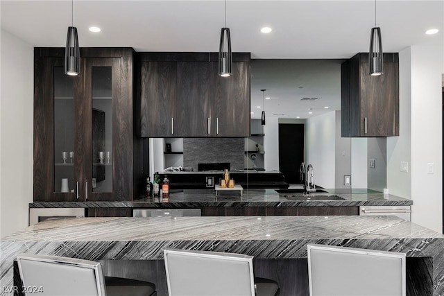 kitchen with kitchen peninsula, a breakfast bar, tasteful backsplash, dark brown cabinets, and sink