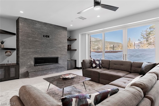 carpeted living room with ceiling fan and a stone fireplace