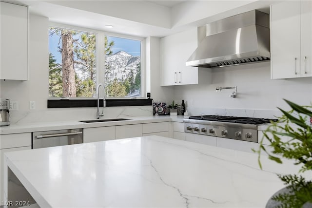 kitchen with wall chimney exhaust hood, white cabinetry, and sink