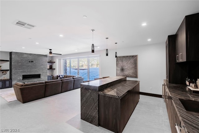 kitchen with light tile flooring, ceiling fan, a center island with sink, a stone fireplace, and built in features