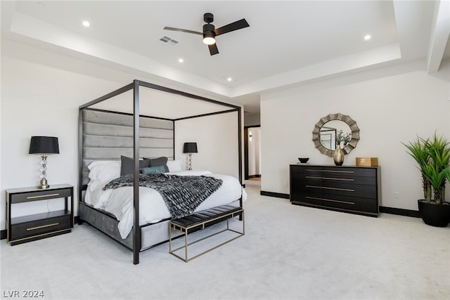 bedroom featuring light carpet, a tray ceiling, and ceiling fan