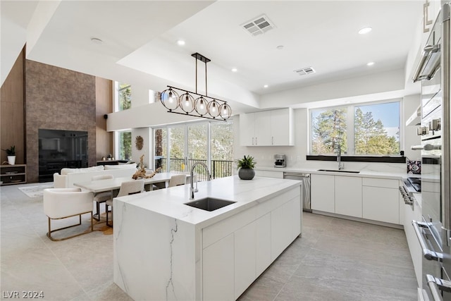 kitchen featuring decorative light fixtures, light stone counters, plenty of natural light, sink, and a large fireplace