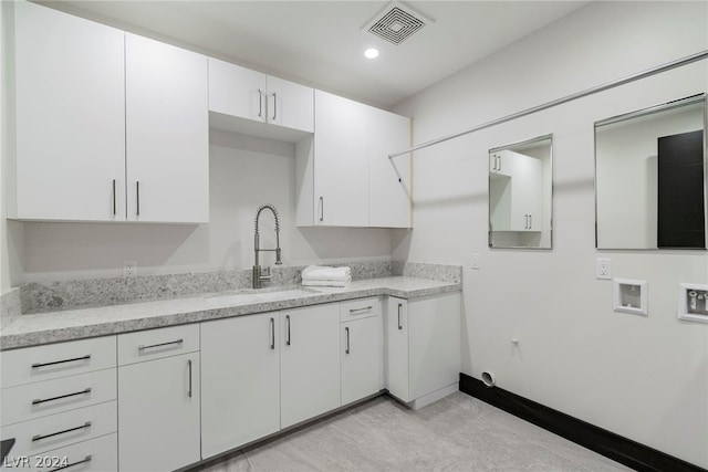 kitchen with white cabinetry, light stone counters, and sink