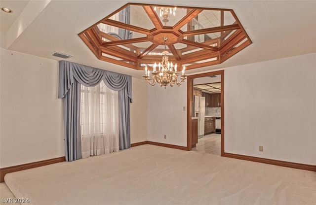 empty room featuring coffered ceiling, a tray ceiling, light carpet, and a notable chandelier