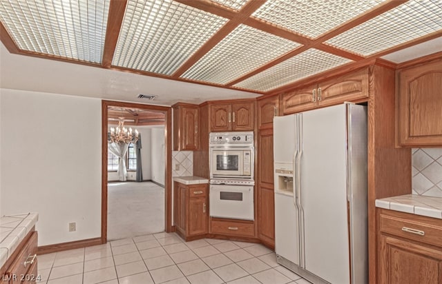 kitchen with white appliances, light tile flooring, tile countertops, tasteful backsplash, and a notable chandelier